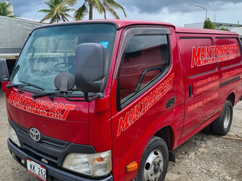 Red Main Transport Toyota van with company signage, parked at the Suva depot under palm trees